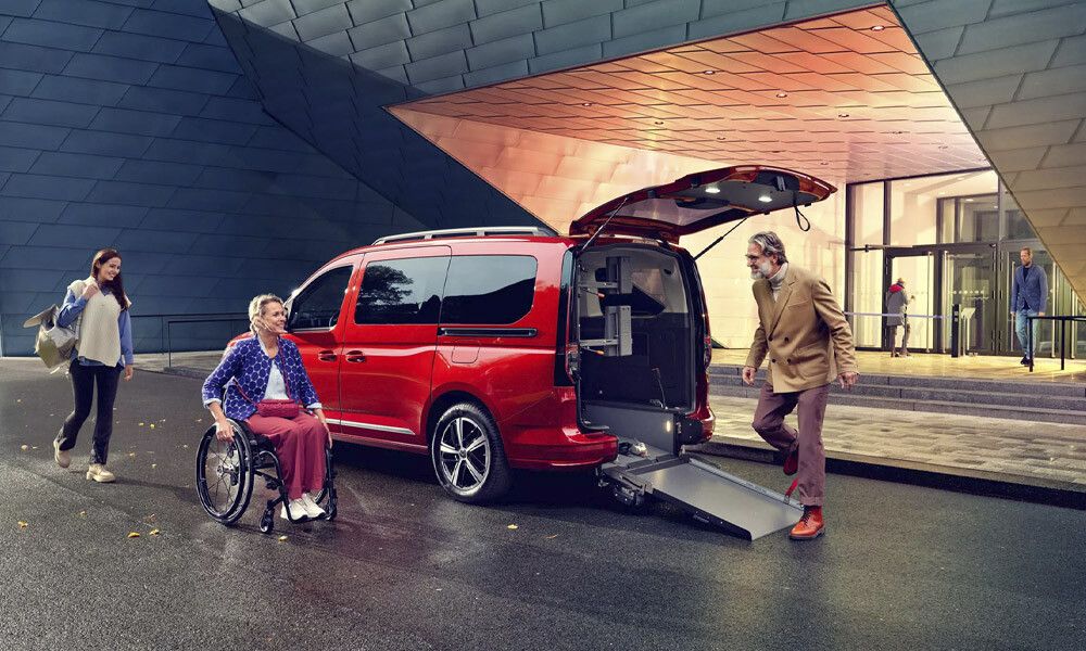 Eine Frau in Rollstuhl nähert sich der praktischen Heckrampe eines VW Caddy