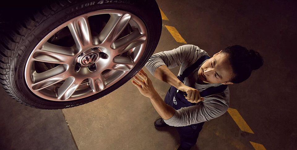 Ein Mitarbeiter führt eine Sichtkontrolle der Räder eines Volkswagens durch.